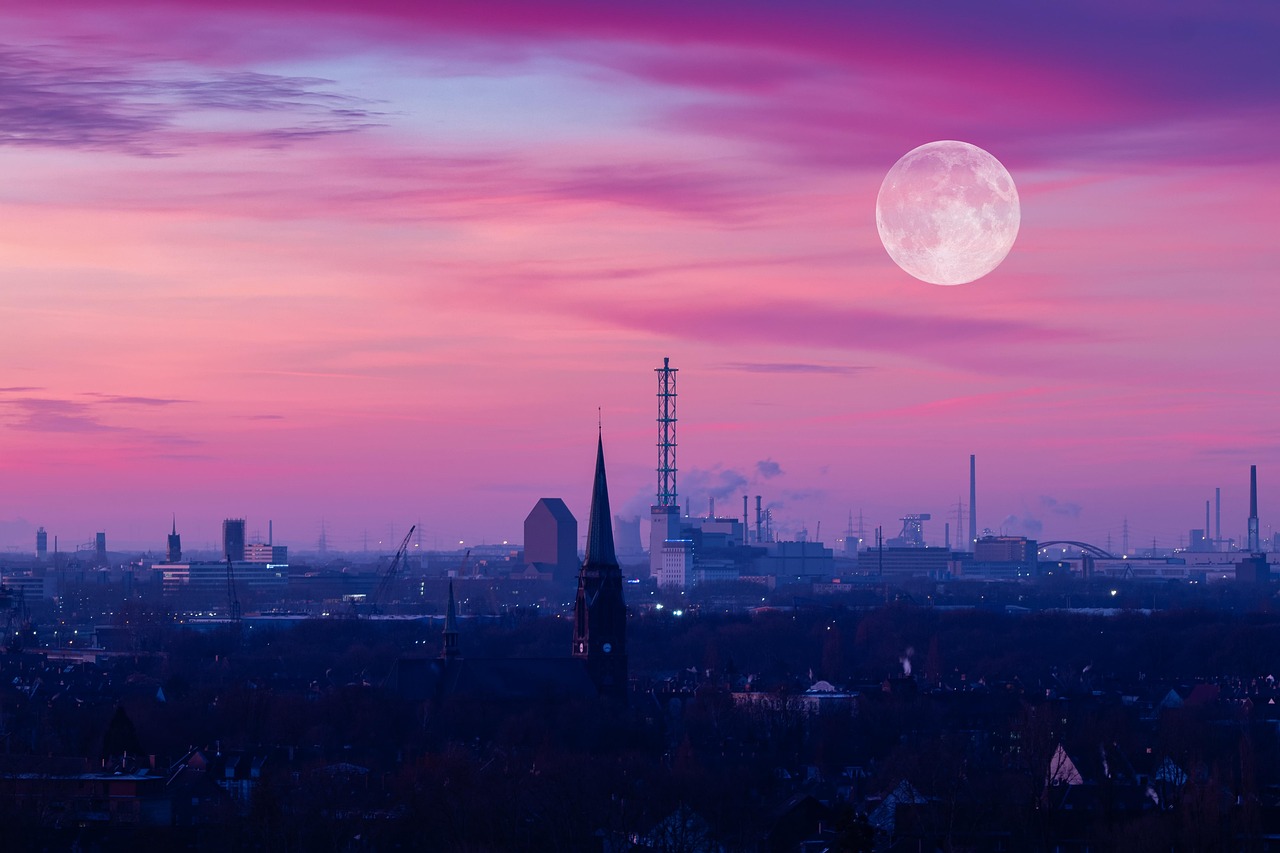 Pembe ve mor gökyüzünde dolunay; aşağıda kent silueti, kuleler ve sanayi yapıları.